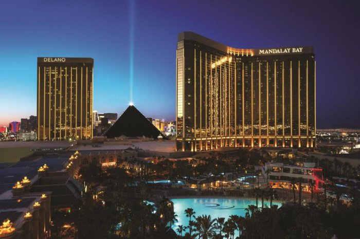 Evening view of Mandalay Bay Resort with illuminated pools and palm trees with Luxor in the background.